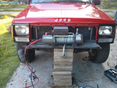 1986 Ford Bronco - A red Jeep Cherokee is shown from the front, a winch mounted to its bumper and a tow rope hanging down.