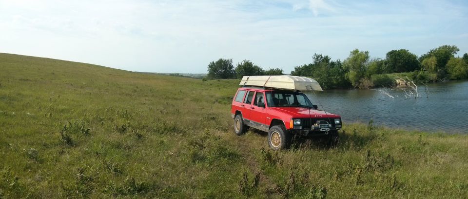 Red Jeep Cherokee with a boat on its roof rack parked by a lake