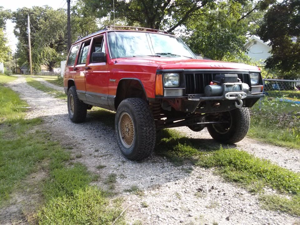 Red Jeep Cherokee XJ with a winch mounted on the front bumper, parked on a gravel driveway