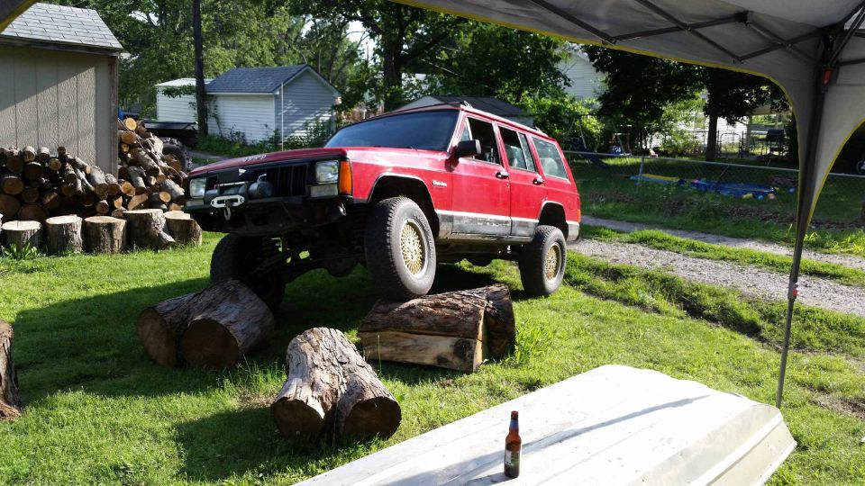 Red Jeep Cherokee XJ with front bumper winch, lifted suspension, and gold wheels