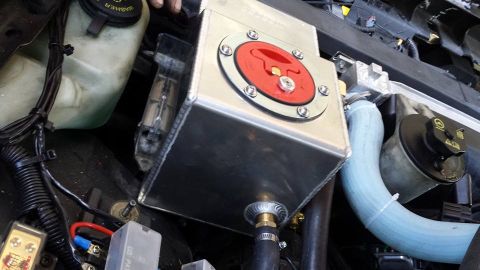 2003 Ford Crown Victoria - Aluminum reservoir tank topped with a red twist-lock fuel-style cap, mounted beside a blue hose in the engine bay.