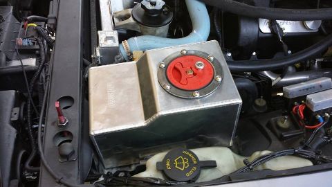 2003 Ford Crown Victoria - Polished aluminum tank with red twist cap sitting above a brake fluid reservoir cap in the engine bay.
