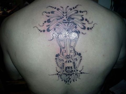 Tattoo of a tribal mask on a person's back, with 'SUPERMOTORS' text in the lower right corner