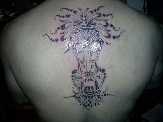 Tattoo of a tribal mask on a person's back, with 'SUPERMOTORS' text in the lower right corner