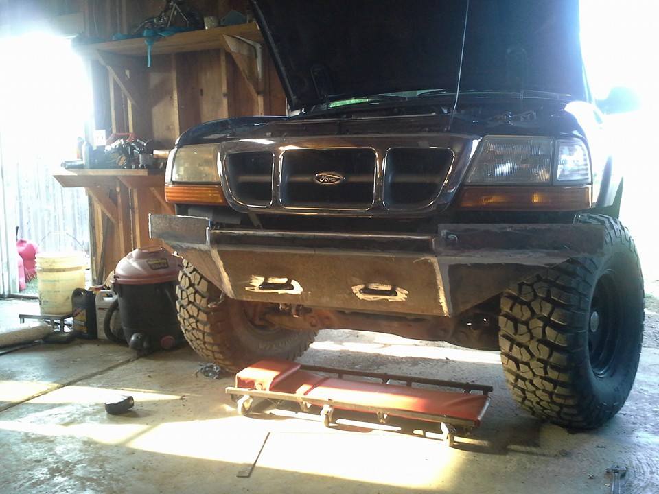 Front view of a black Ford Ranger with a custom metal bumper and large tires. The hood is open, and it's in a garage setting