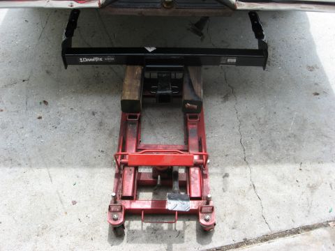1994 Ford Bronco - Receiver hitch assembly supported by a red floor jack and wooden blocks on a concrete surface.