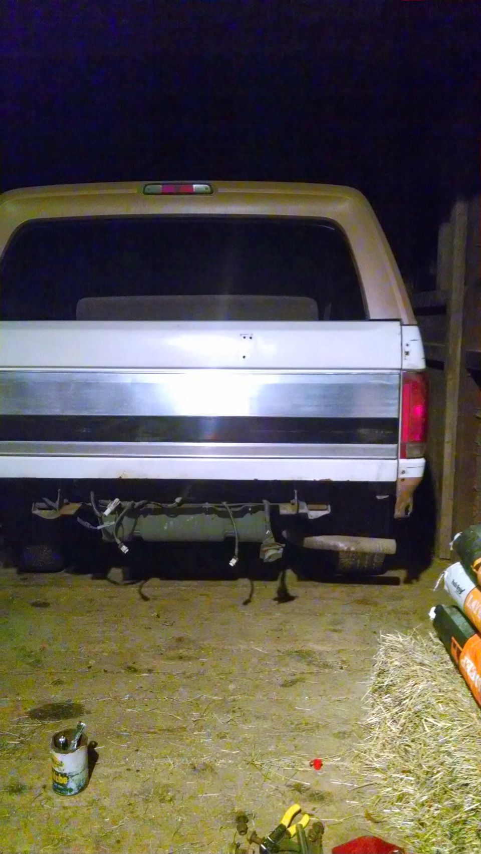 Rear of a tan and white Ford Bronco, missing its bumper and showing exposed wiring