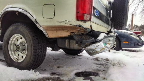 1995 Ford Bronco - The rear bumper of a Ford Bronco is heavily damaged, with a spare tire mounted on the tailgate.