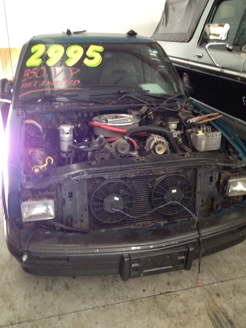 Green pickup truck with hood open, showing engine and fans. Price tag on windshield says 2995