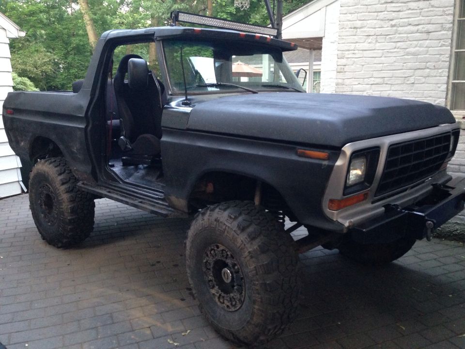 Modified black Ford Bronco with off-road tires and a light bar. Doors removed, showing interior seats