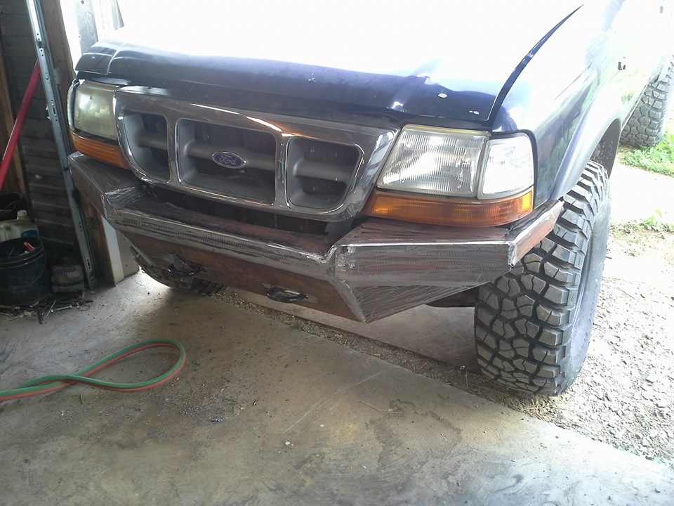Custom metal front bumper on a dark blue truck with aggressive tires