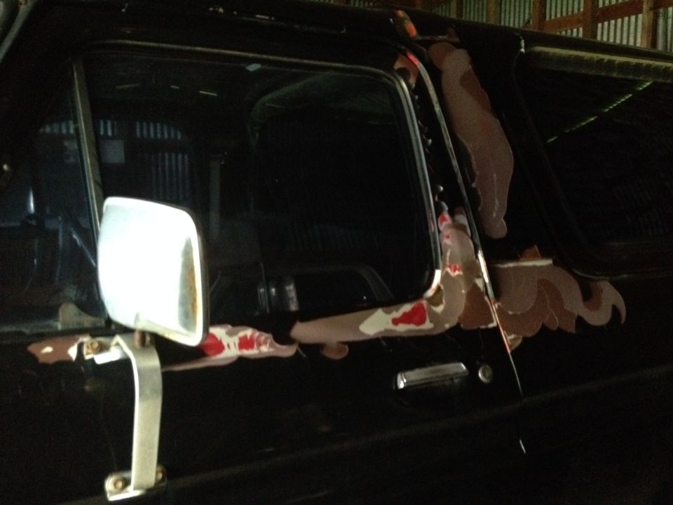 Side view of a black vehicle's door and mirror. Paint is chipped and showing primer