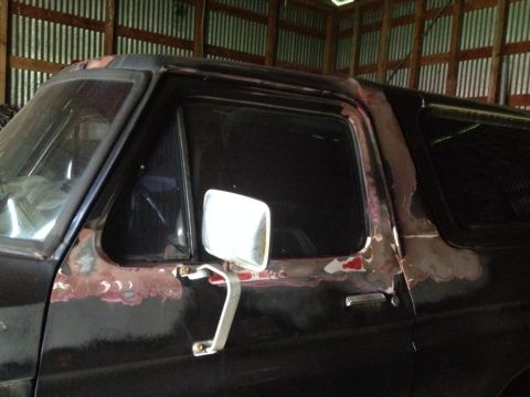 1978 Ford Bronco - The side of a black 1978 Ford Bronco is visible, with areas of rust and primer on the body panels.