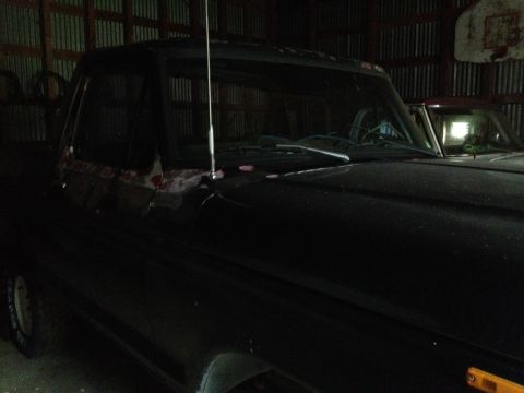 1978 Ford Bronco - A black truck cab and hood are visible in a dimly lit garage with another vehicle behind it.