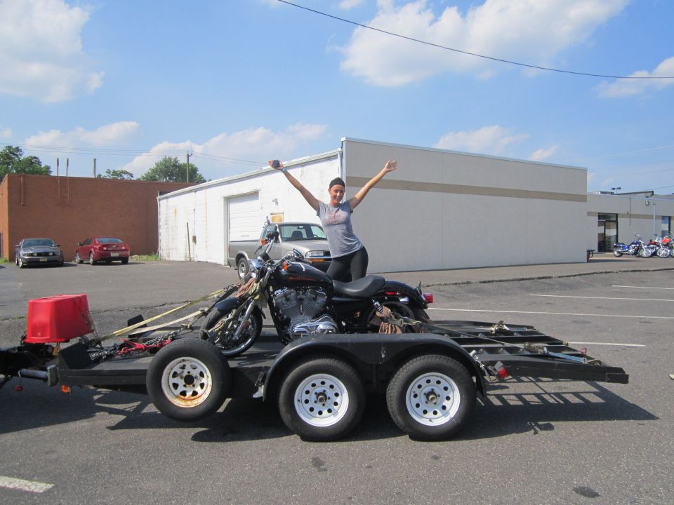 Woman with arms raised standing on a motorcycle loaded onto a trailer