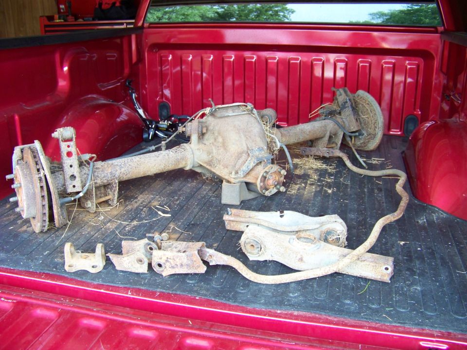 Rusty rear axle assembly and suspension components in a red pickup truck bed