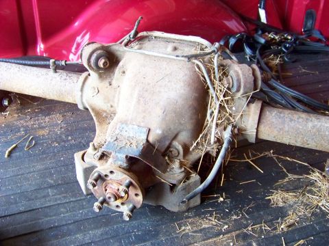 1999 Mercury Grand Marquis - A used rear axle assembly is shown, covered in straw and debris, resting in the cargo area of a vehicle.