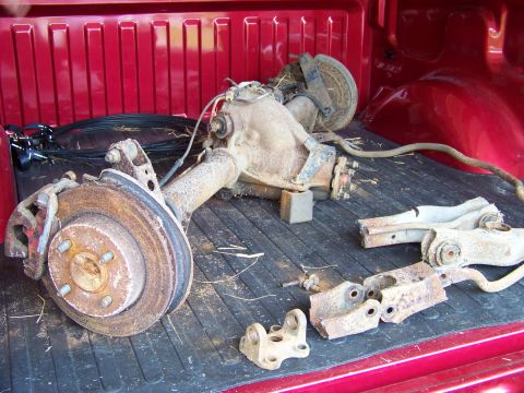 1999 Mercury Grand Marquis - Various rusty automotive axle and suspension parts are laid out in the bed of a red pickup truck.