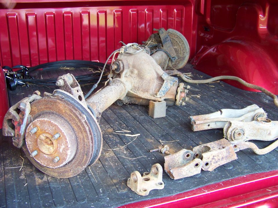 Rusty rear axle assembly with brake rotors and suspension parts in a red truck bed