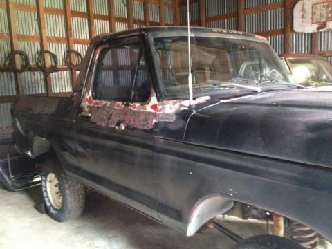 1978 Ford Bronco - A black pickup truck with visible rust and damage sits in a garage.