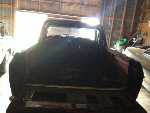 1978 Ford Bronco - The rear interior of a red pickup truck is visible, with another vehicle parked to the left and a white car to the right.