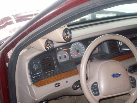 2004 Ford Crown Victoria - The interior of a 2004 Ford Crown Victoria shows a tan dashboard with added gauges and a Ford steering wheel.