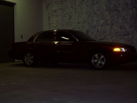 2004 Ford Crown Victoria - A dark red 2004 Ford Crown Victoria is parked inside a garage with a stone wall in the background.