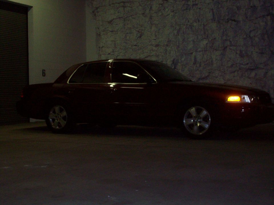 Dark red 2004 Ford Crown Victoria sedan parked indoors, three-quarter front view, with chrome wheels and illuminated turn signal