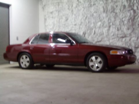 2004 Ford Crown Victoria - A red 2004 Ford Crown Victoria sedan is parked indoors, showing its side profile.