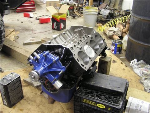 1993 Ford Bronco - An engine block and its newly painted blue water pump sit on blocks in a cluttered garage workshop.