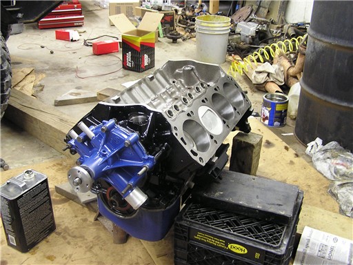 V8 short block with blue timing cover and oil pan, open lifter valley, on a garage floor