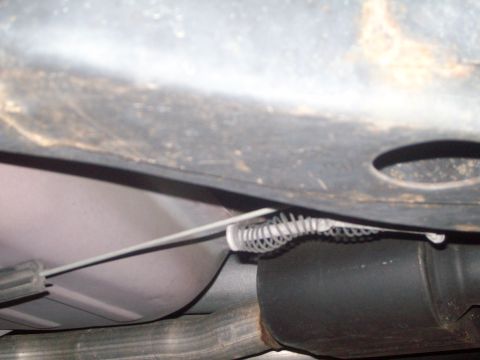 2004 Ford Crown Victoria - Close-up view of the undercarriage of a vehicle, showing the exhaust system and a control cable.