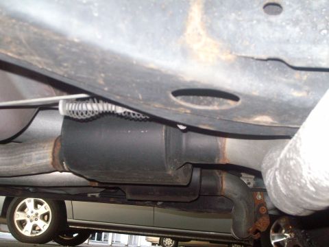 2004 Ford Crown Victoria - Undercarriage view of a vehicle, showing exhaust system parts and a wheel. Another car is visible underneath.