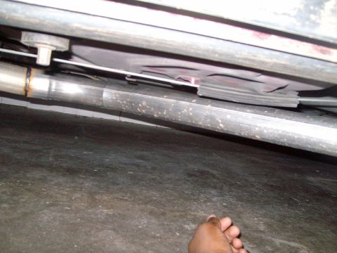 2004 Ford Crown Victoria - The underside of a vehicle, showing the exhaust system and frame components. A hand is visible in the lower right corner.