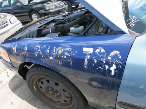 1991 Ford LTD Crown Victoria - A blue police car fender shows faded white lettering and markings, with the hood open revealing the engine.