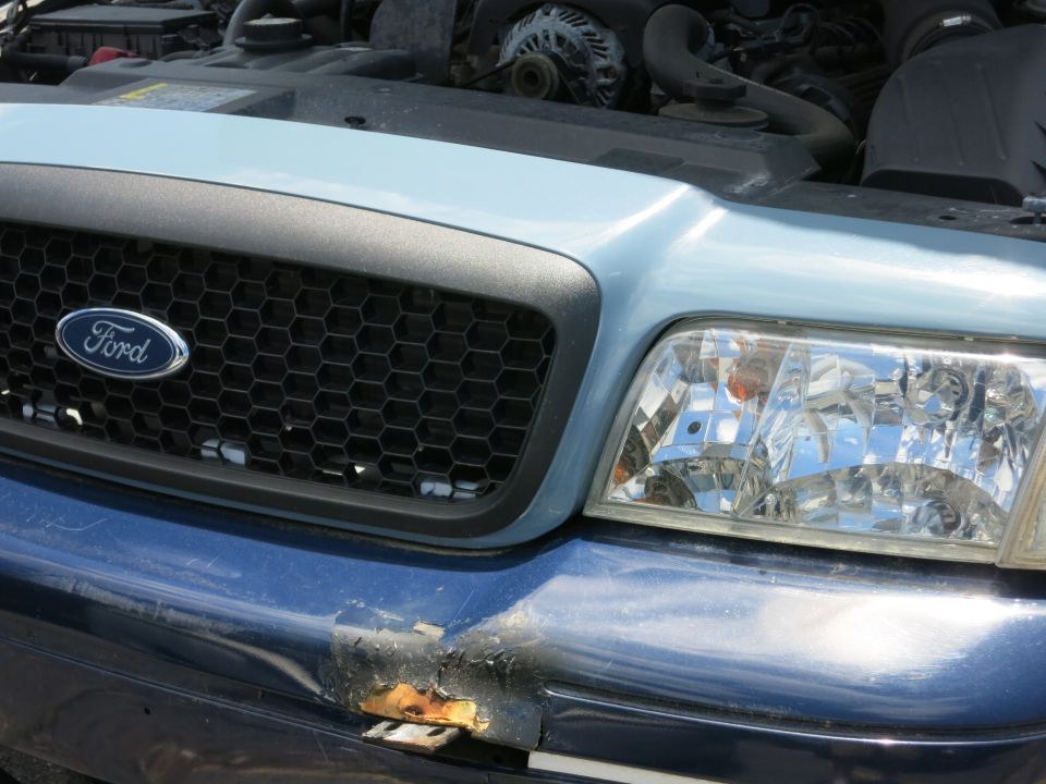 Ford Crown Victoria front grille and headlight with damaged bumper. Engine visible under hood