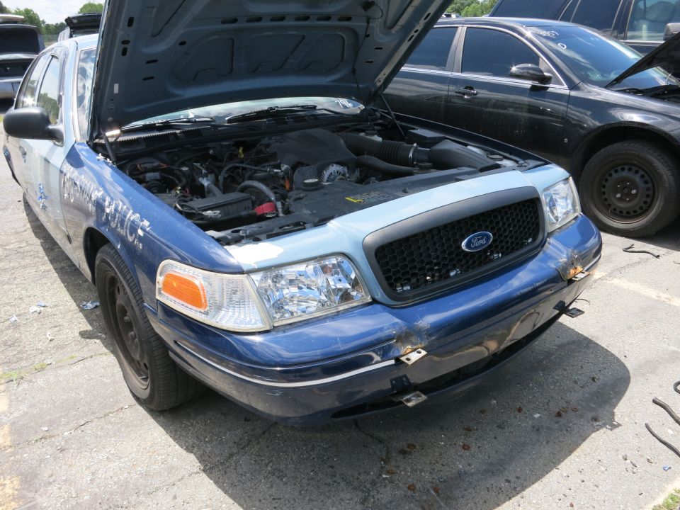 Blue and white Ford Crown Victoria police car with hood open, showing engine. Another car is parked behind it
