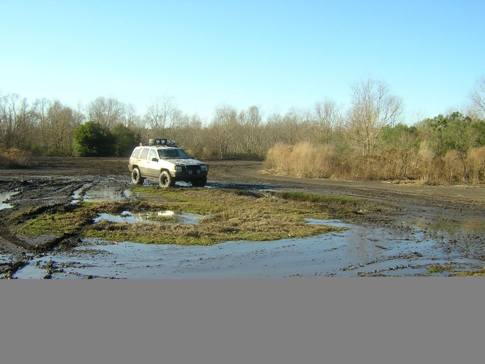 White Jeep Grand Cherokee with roof rack driving through muddy terrain
