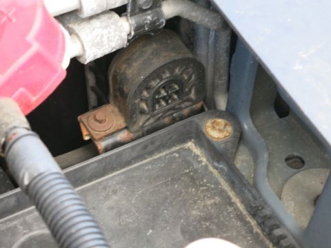 1991 Ford LTD Crown Victoria - A close-up view of a vehicle's engine compartment shows a black plastic component secured by a rusty metal bracket.