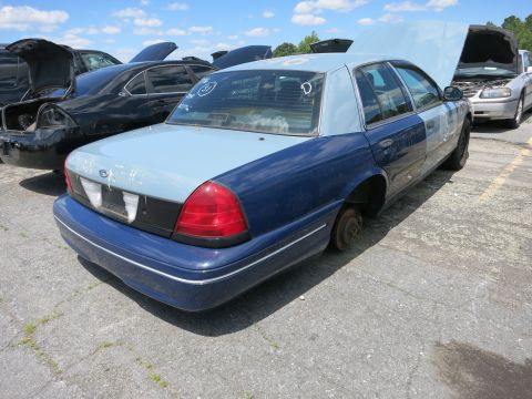 1991 Ford LTD Crown Victoria - A two-tone Ford Crown Victoria sits in a junkyard with one wheel missing and its hood open.