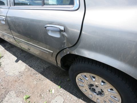 1991 Ford LTD Crown Victoria - The rear passenger side door of a gray sedan shows damage and a dented area near the wheel well.