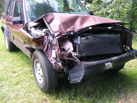 Damaged maroon SUV front end with exposed radiator and crumpled hood