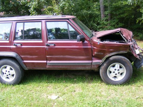 Maroon Jeep Cherokee XJ with severe front-end damage, parked on grass
