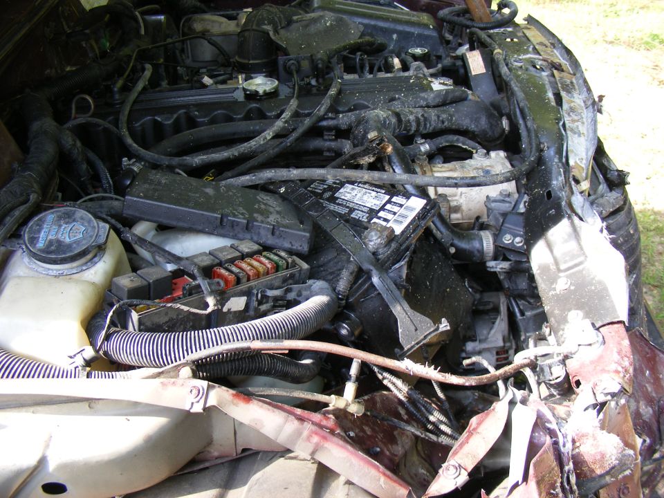 Engine bay of a damaged vehicle, showing battery, fuse box, and engine components