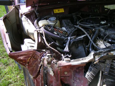 Engine bay of a wrecked maroon vehicle, showing damage to the front fender and engine components