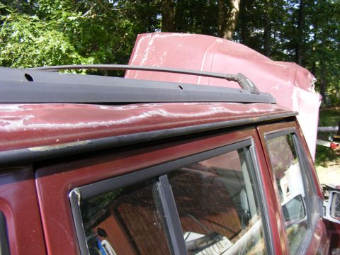 Red SUV roof rack with peeling paint on the roof. Another red vehicle part is visible behind it