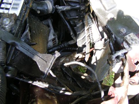 Close-up of a damaged engine bay with hoses and wires visible
