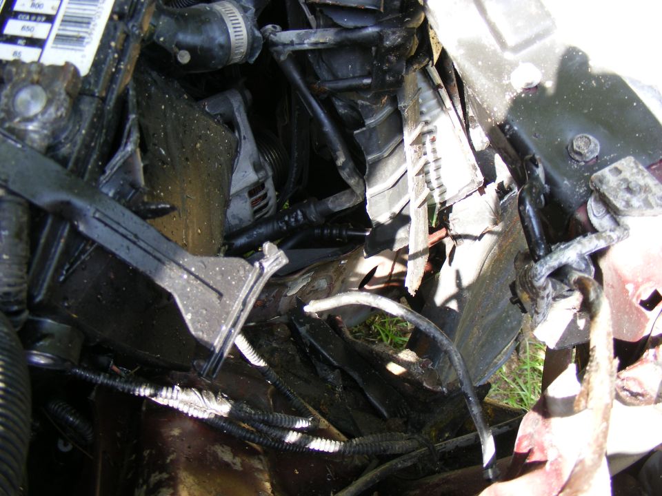 Close-up of a damaged engine bay with hoses and wires visible