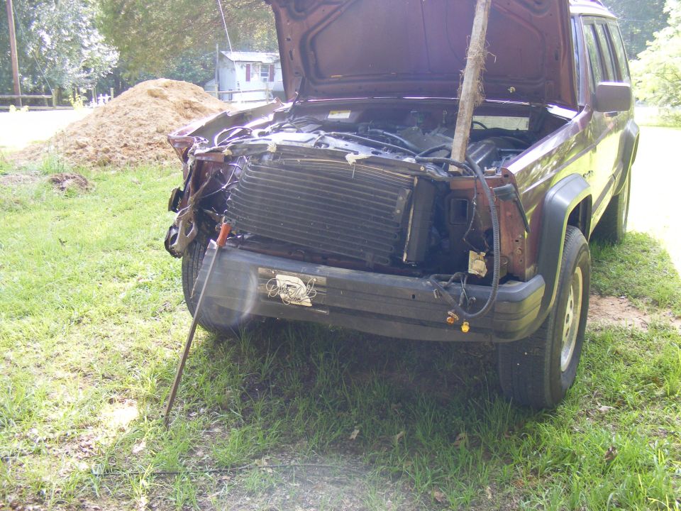 Maroon Jeep Cherokee XJ with damaged front end, hood open, and a stick propping it up