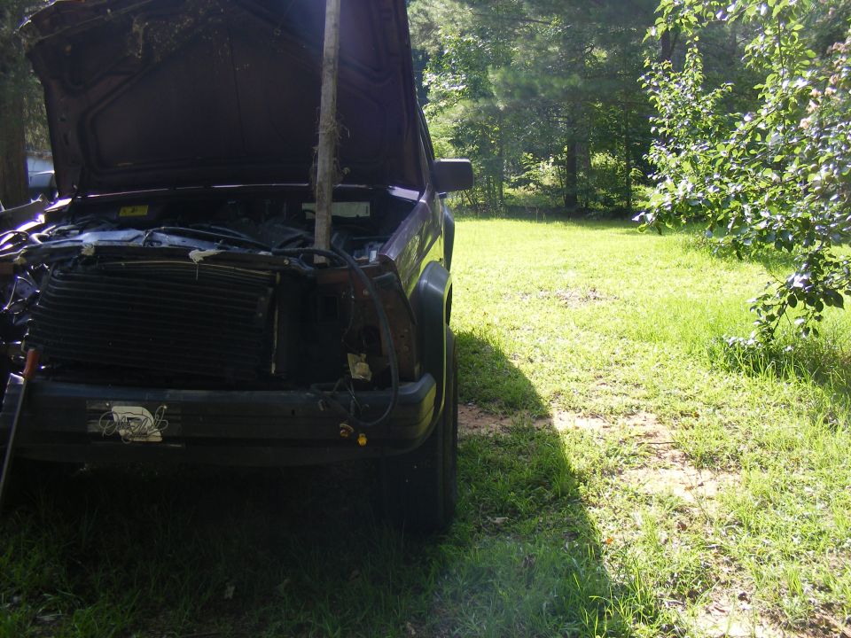 Front view of a dark SUV with hood open, showing a damaged grille